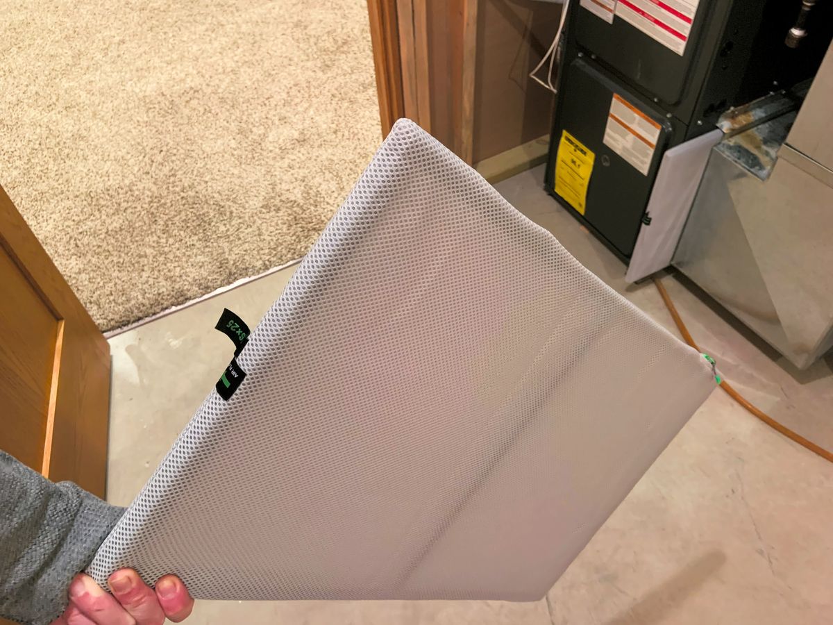 Reusable HVAC air filter held up in front of a furnace