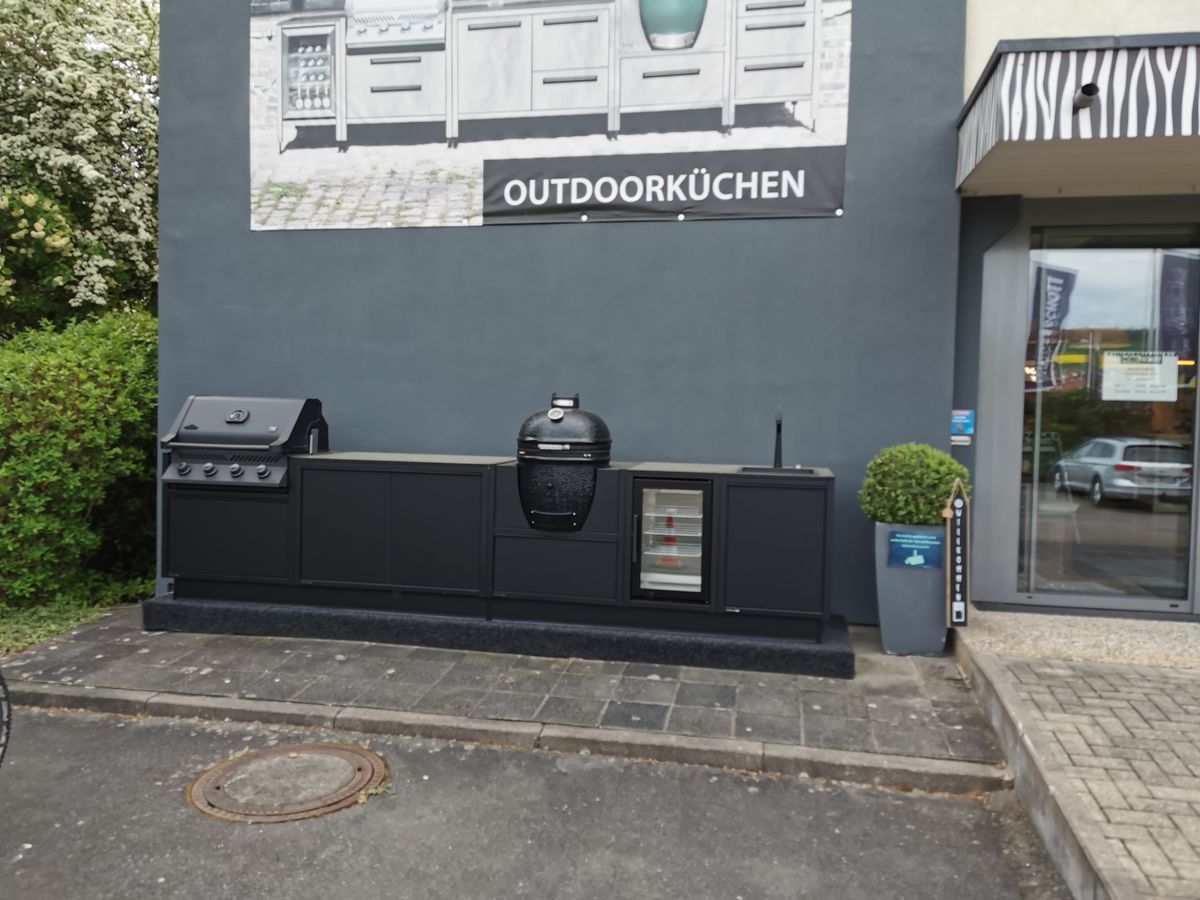 Outdoor kitchen display unit with a grill, storage cabinets, and a refrigerator