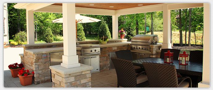 A covered outdoor kitchen with stone counters, grill, and dining area