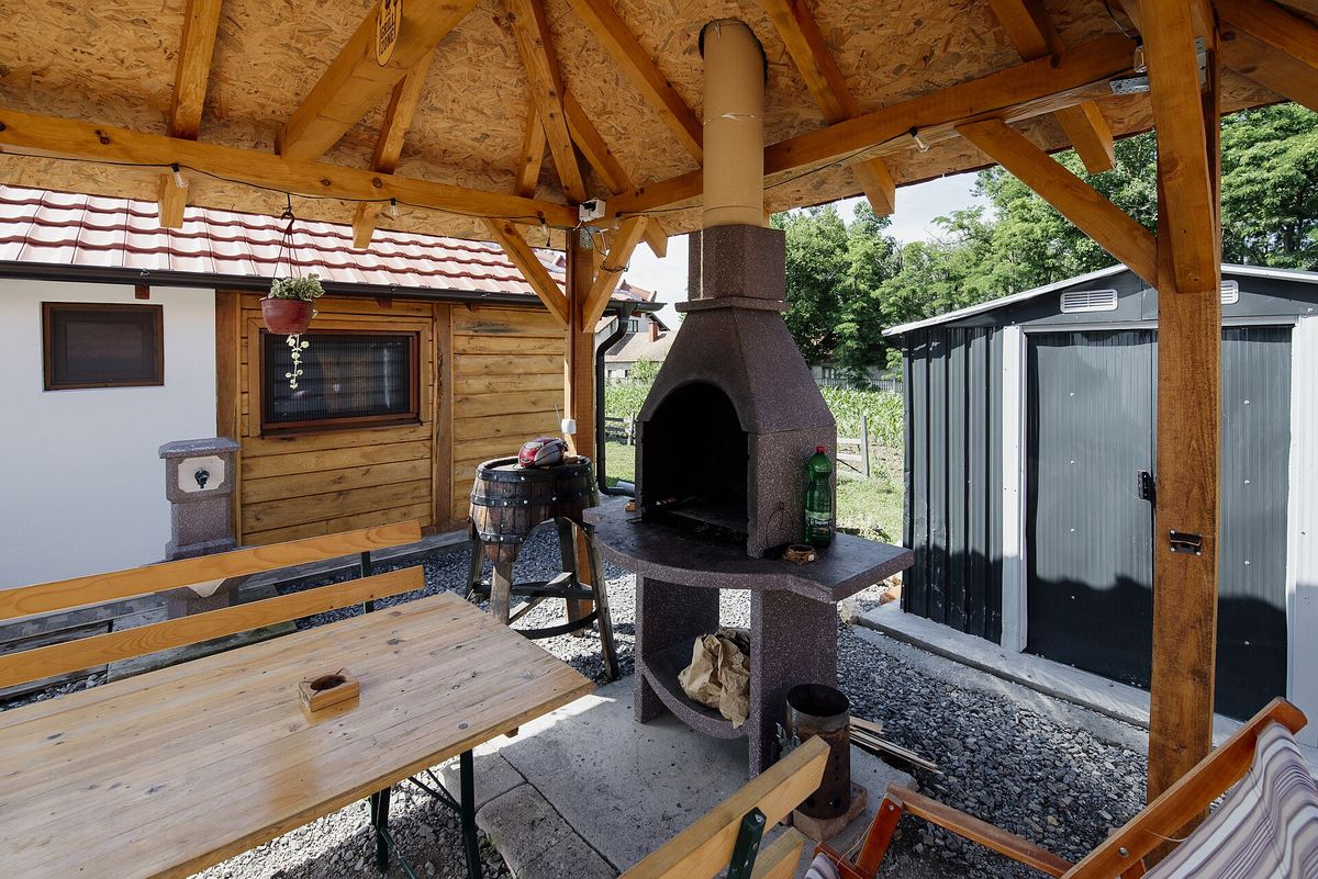 Covered outdoor cooking area with a stone grill fireplace and wooden tables