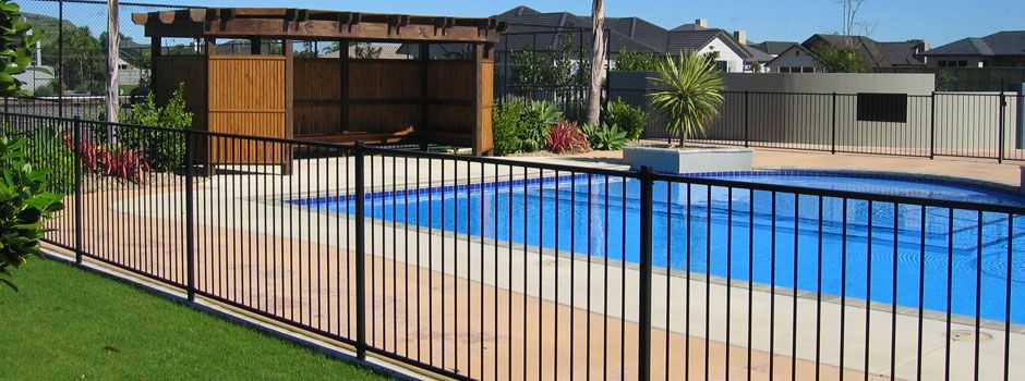 Black metal pool safety fence around a backyard swimming pool