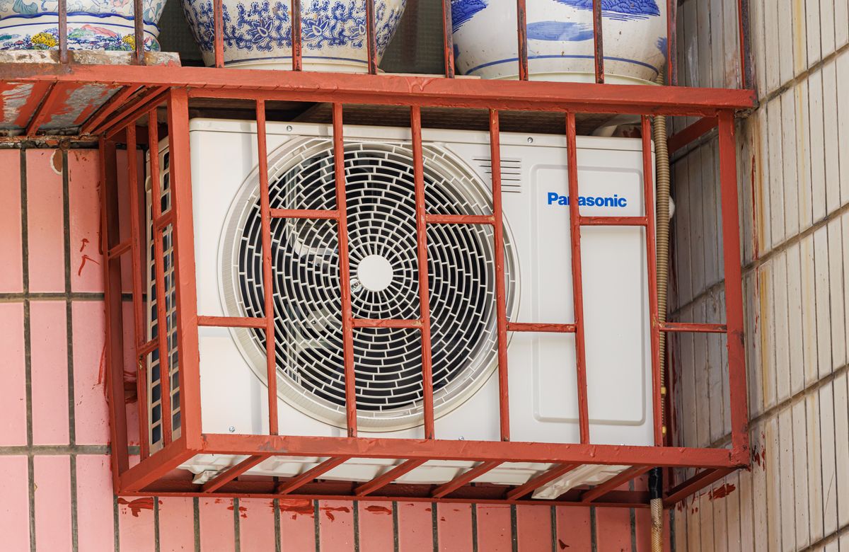 Outdoor air conditioner condenser unit mounted behind a protective metal cage