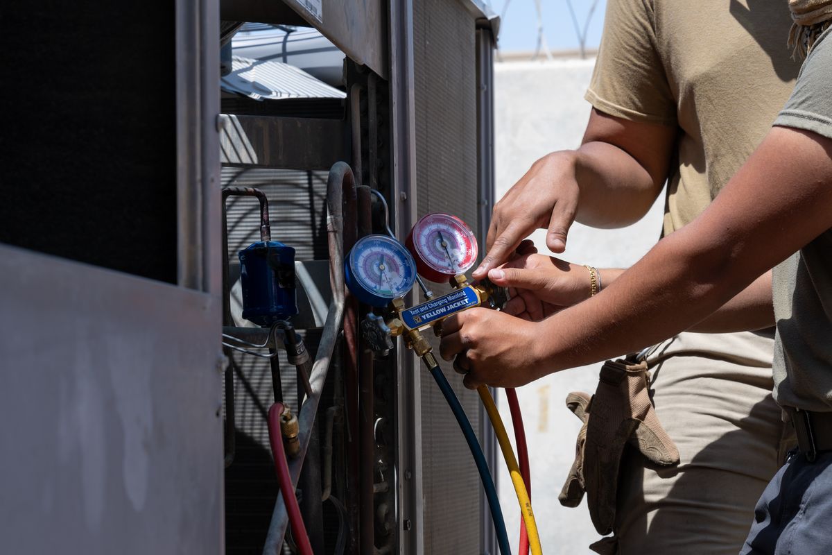 An HVAC technician using a pressure gauge to inspect an air conditioning unit