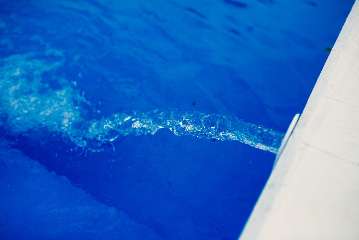 Clear stream of water flowing into a bright blue swimming pool